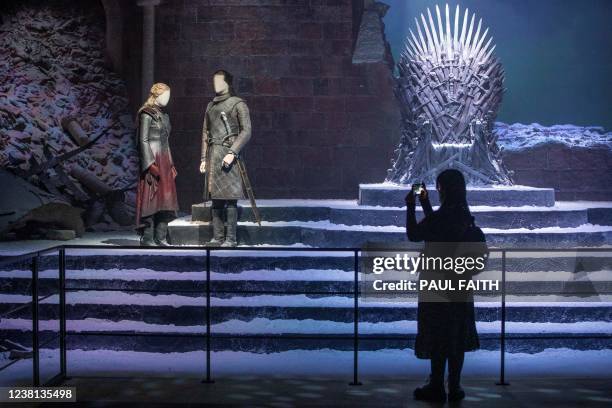 Visitor takes pictures of a "Game of Thrones" set featuring the Iron Throne and statues of characters Daenerys Targaryen and Jon Snow during a press...