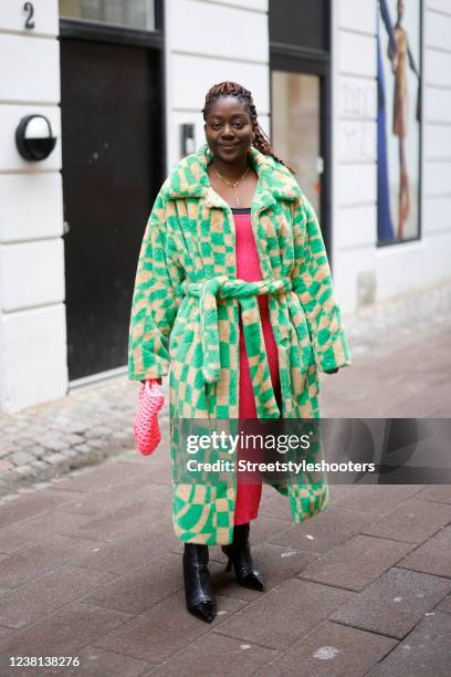 Influencer Lois Opoku wearing black boots by Jimmy Choo, a pink maxi dress by Ganni, a beige and green long coat by Monki and a pink bag by Maiami,...