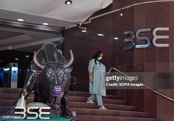 Woman wearing a protective face mask walks past a statue of a bull inside the Bombay Stock Exchange building in Mumbai. Stock prices rise if the...