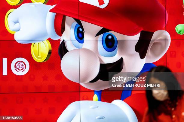 An employee wearing a face mask stands next to a screen displaying a character of Nintendo game Super Mario at a store for Japanese games giant...
