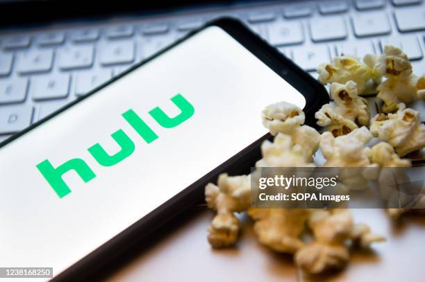 In this photo illustration a Hulu logo seen displayed on a smartphone with popcorns and laptop keyboard in the background.