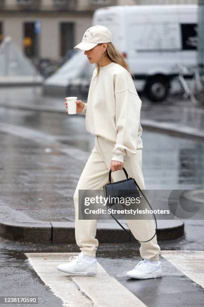 Influencer Alessa Winter wearing a beige pullover by LeGer, beige sweatpants by LeGer, a black bag by Balenciaga, a beige cap by LeGer and white...