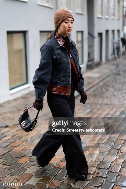 Betty Bachz wearing a black denim jacket by Tomorrow Denim, a brown knitted beanie, a brown leather jacket by Holzweiler, black pants and a black bag...