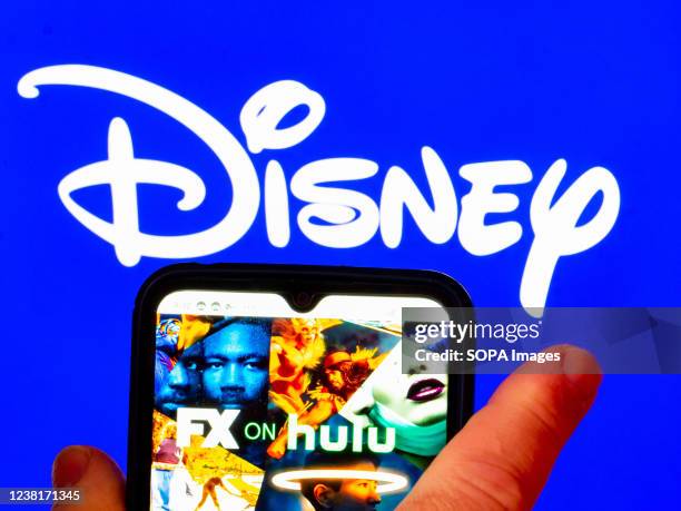 In this photo illustration, the FX on Hulu logo is displayed on a smartphone screen with a Disney logo in the background.