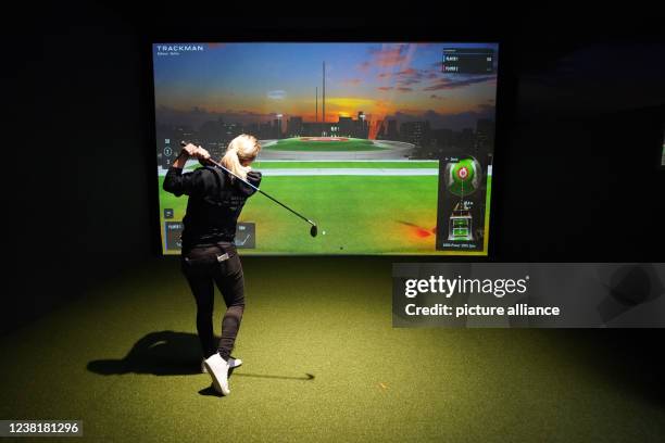 February 2022, Schleswig-Holstein, Glinde: A woman hits a ball in a golf simulator at the "Eisen Sieben" indoor golf facility. After finishing his...