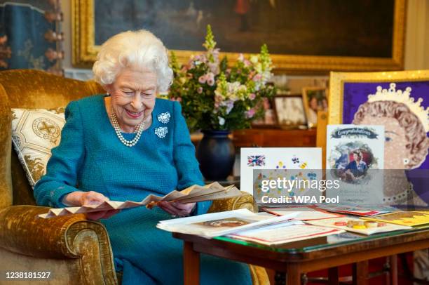 Queen Elizabeth II looks at a fan as she views a display of memorabilia from her Golden and Platinum Jubilees in the Oak Room at Windsor Castle on...