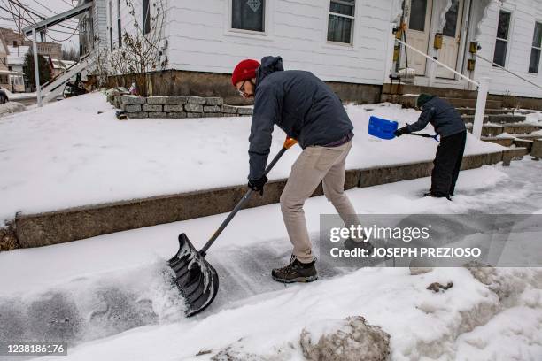 Father and son shovel sleet from the sidewalk during a winter storm in Concord, New Hampshire on February 4, 2022. - The winter storm stretched from...