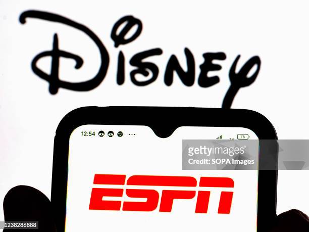 In this photo illustration, the ESPN logo is displayed on a smartphone screen with the Disney logo in the background.