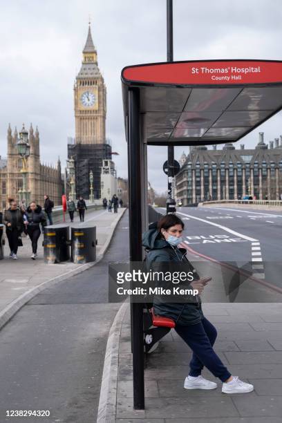 Woman wearing a face mask as a precaution against Coronavirus / Covid-19 sits at a bus stop on Westminster Bridge near the Houses of Parliament on...
