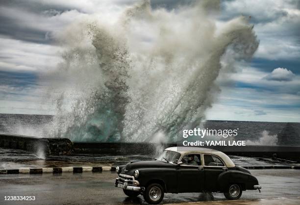 An old American car drives as strong wind pushes a wave in Havana malecon, on February 9, 2022.