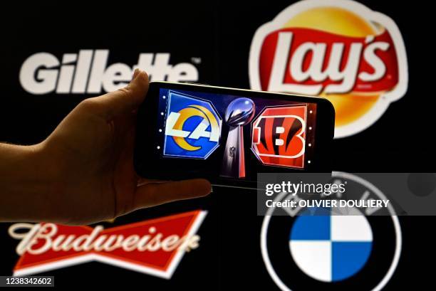 This illustration photo shows the logos of the Cincinnati Bengals and the Los Angeles Rams on a phone in front of the Gillette, Lays, Budweiser and...