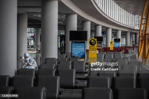 Member of staff wearing full personal protective kit checks their phone as they wait in an almost completely empty departure hall at Beijing Capital...
