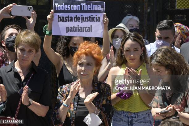 Argentine actress Thelma Fardin applauds next to actress Mirta Busnelli as another actress holds a sign reading "All with Thelma, enough of...
