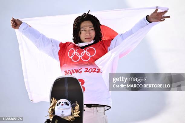 Gold medallist Japan's Ayumu Hirano holds his national flag on the podium during the venue ceremony after the snowboard men's halfpipe final run...