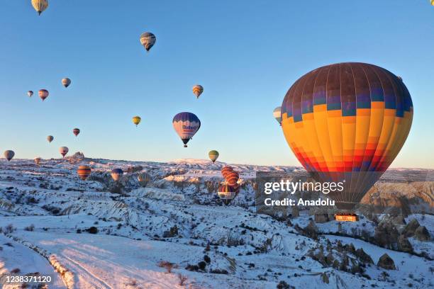 Hot-air balloons glide over snow-covered fairy chimneys in the Cappadocia region during sunrise, located in Nevsehir, Turkiye on February 11, 2022....