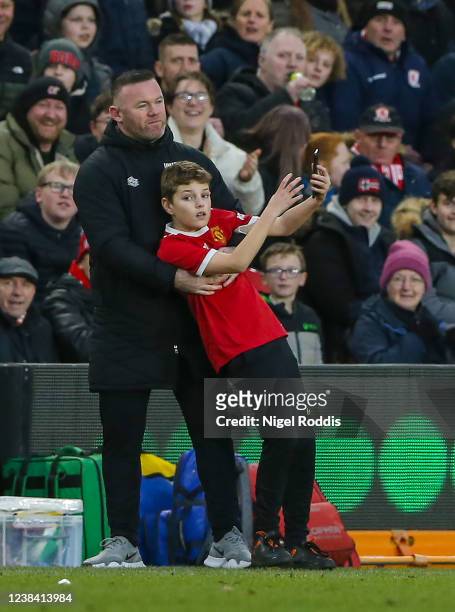Young fan enters the technical area to take a selfie with Wayne Rooney manager of Derby County during the Sky Bet Championship match between...
