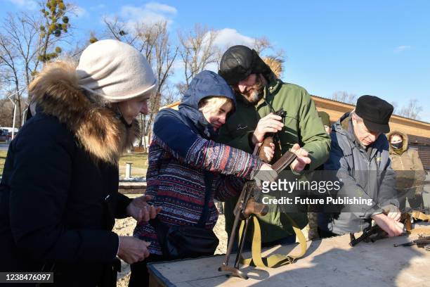 Participant of an open civil defence drill helps a woman to assemble an AK-74 automatic rifle in metropolitan Hydropark, Kyiv, capital of Ukraine