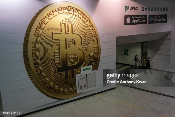 Pedestrians walk past an advertisement displaying a Bitcoin cryptocurrency token on February 15, 2022 in Hong Kong, China. Cryptocurrencies are...