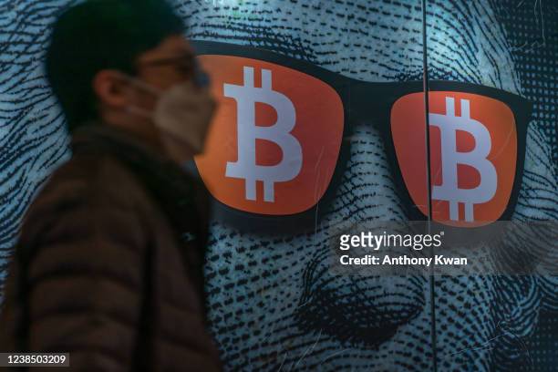 Pedestrians walk past a display of cryptocurrency Bitcoin on February 15, 2022 in Hong Kong, China. Cryptocurrencies are gaining popularity worldwide...
