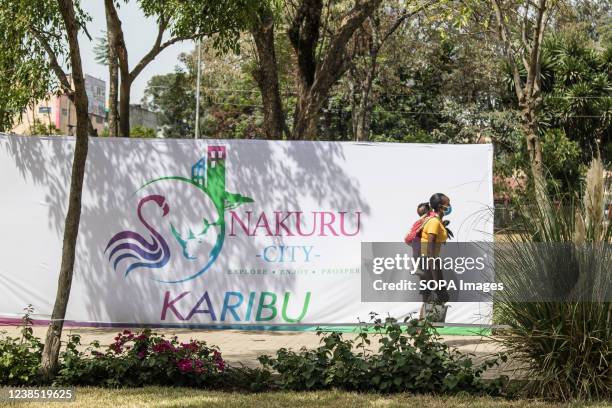 Mother carrying a baby on her back walks past a banner of Nakuru City at Nyayo Garden in the Central Business District. Nakuru municipality was...