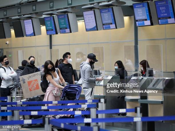 Travelers wearing face masks line up in front of the airline counters at Vancouver International Airport in Richmond, British Columbia, Canada, on...