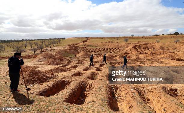 Libyans walk arround graves dug on the ground from which bodies were recovered in the western town Tarhuna on February 9, 2022. For years a brutal...