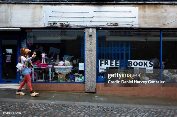 Person wearing a brightly coloured and furry animal costume passes a vacant and disused charity shop with a sign in the window that says "free books"...