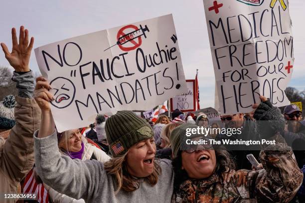 Two activists who refuse to give their names hold up their signs as activists and faith groups protest against COVID-19 vaccine mandates and...