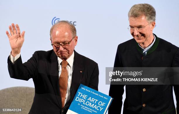 Outgoing Munich Security Conference Chairman Wolfgang Ischinger stands next to his designated successor Christoph Heusgen and holds a book titled...