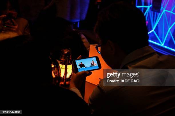 People watch on a mobile phone a live footage of the closing ceremony of Beijing 2022 Winter Olympics Games, at a bar in Beijing on February 20, 2022.