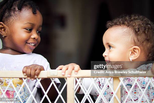 two toddlers looking at each other and smiling - baby gate imagens e fotografias de stock