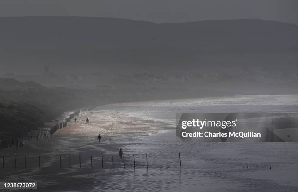 Walkers are seen walking through sea foam gathered on the beach as a result of Storm Franklin on February 21, 2022 in Portstewart, United Kingdom....