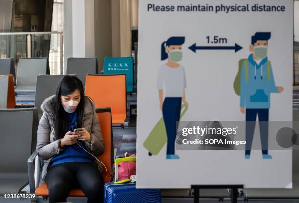 Passenger sits next to a sign reminding people to keep social distancing at Hong Kong's Chek Lap Kok International Airport. Hong Kong is notoriously...