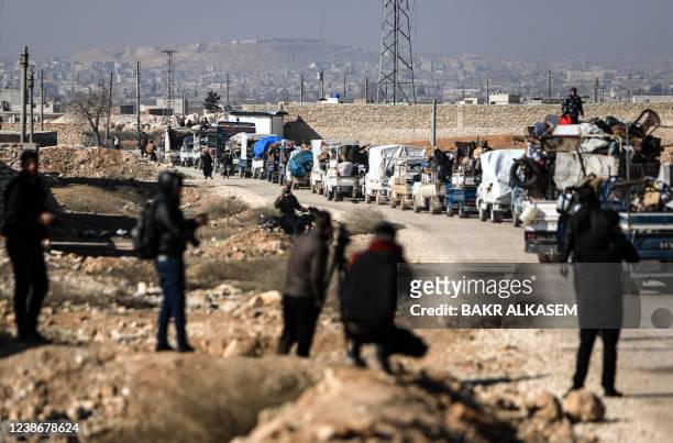 People watch as a convoy of trucks transports internally displaced Syrians and their belongings to a new housing complex in the opposition-held area...