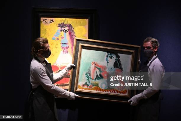 Gallery assistants hold an artwork entitled "Nu assis sur un tapis rayé" next to "Buste d'homme" by Spanish artist Pablo Picasso during a photocall...