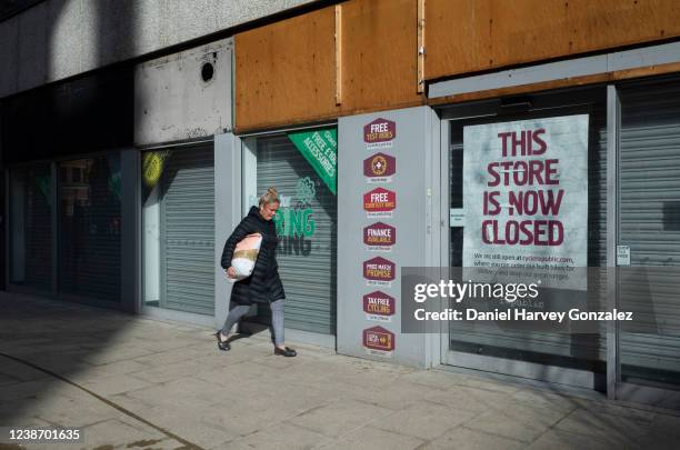 Woman holding a large parcel under her arm walks past a permanently closed high street shop with a sign in the window detailing the store's move to...