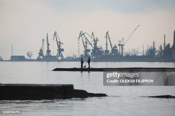 Couple walks a dog on a pier at a coast of the Sea of Azov in Ukraine's industrial port city of Mariupol on February 23, 2022. Mariupol lies on the...