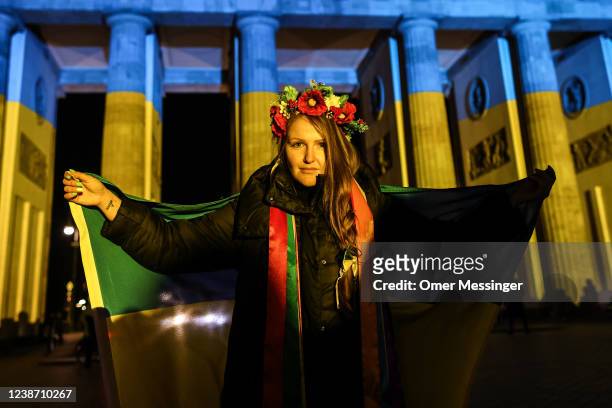 Woman holds a flag in fron of the Brandenburg Gate, as it is lit in the blue and yellow colours of the Ukrainian national flag in solidarity with...
