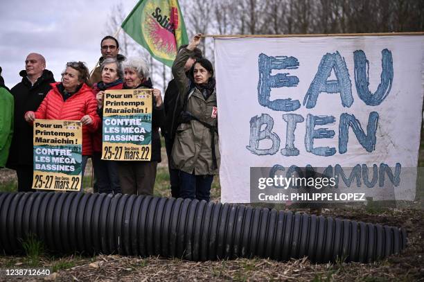 Men and women hold placards and a banner reading "Water common good" next to a water pipe linked to a mega pong during a gathering against the first...