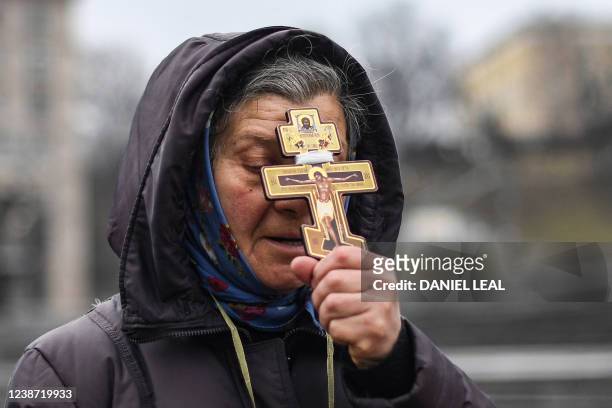 Religious woman holds a cross as she prays on Independence square in Kyiv in the morning of February 24, 2022. Air raid sirens rang out in downtown...