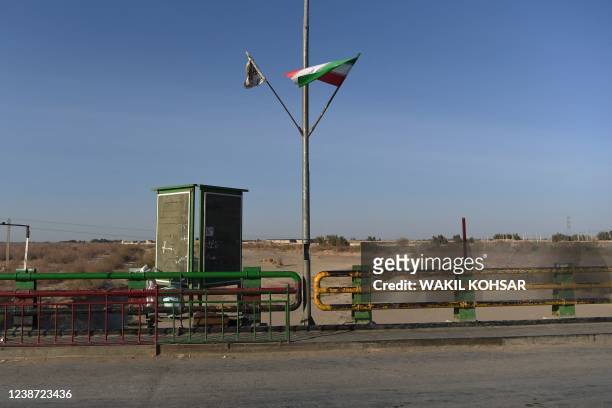 In this photo taken on February 18, 2022 a Taliban flag and an Iranian flag wave at the zero point of Afghan-Iran border crossing bridge in Zaranj.