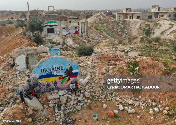 This aerial view shows a mural amid the destruction, depicting the colours of the Russian and Ukrainian flags, painted by Syrian artists to protest...