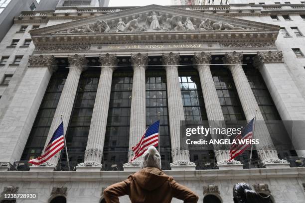 Person stands in front of the New York Stock Exchange at Wall Street on February 24, 2022 in New York. - Wall Street stocks opened sharply lower...