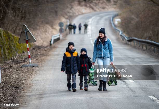 Woman with two children and carrying bags walk on a street to leave Ukraine after crossing the Slovak-Ukrainian border in Ubla, eastern Slovakia,...