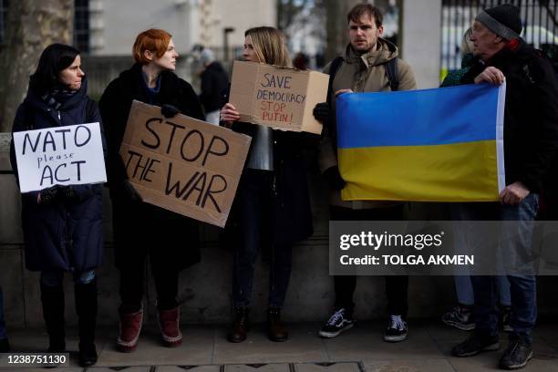 Demonstrators hold placards reading "NATO please act", "Stop the war" and "Save democracy, stop Putin" as they stand next to two other participants...