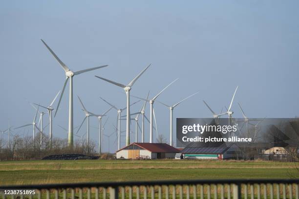 February 2022, Schleswig-Holstein, Hattstedtermarsch: Wind turbines stand in a field behind a farm. A hall roof is equipped with solar panels and...