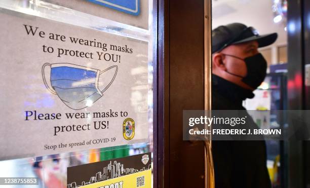 Man wears his mask as he walks past a sign posted on a storefront reminding people to wear masks, on February 25, 2022 in Los Angeles, - Los Angeles...