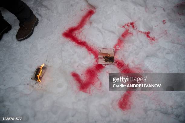 Burning Russian passport is left on the snow with a painted swastika as members of the Ukrainian community protest in front of the Consulate General...