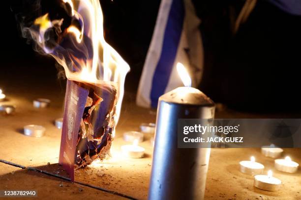 Russian passport set aflame is placed next to burning candles during a protest against Russia's military operation in Ukraine, in front of the...