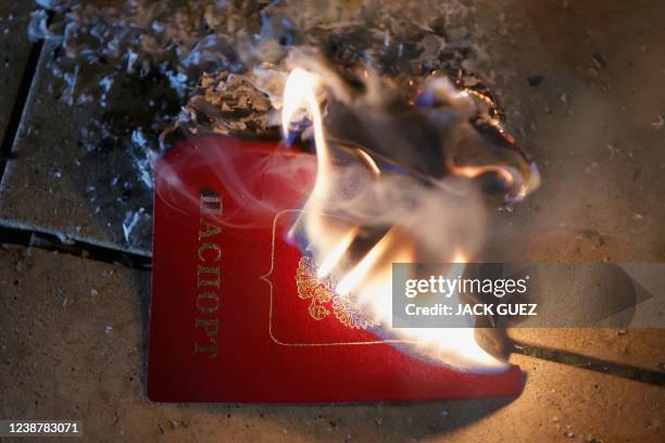 Russian passport set aflame is placed next to burning candles during a protest against Russia's military operation in Ukraine, in front of the...